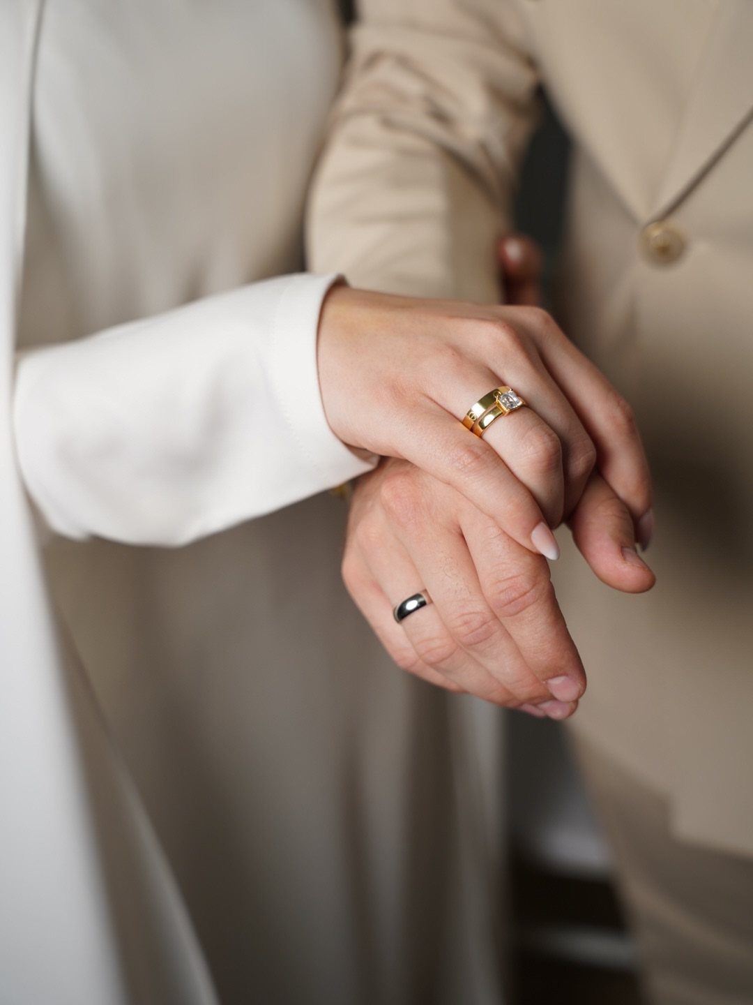 Stacked hands of a couple showing a gold diamond ring and silver band.