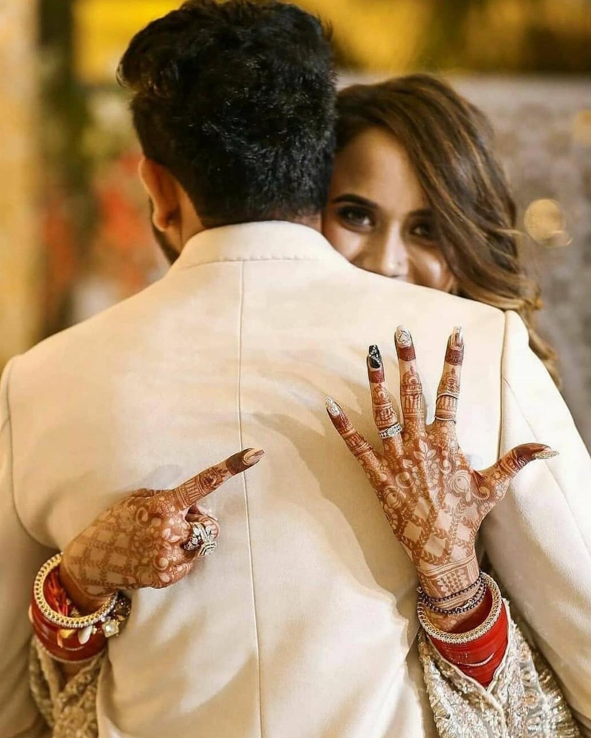 Woman with henna hands and rings resting them on a man's white jacket