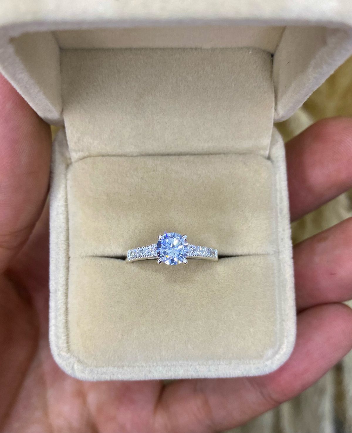 Diamond engagement ring resting inside a beige velvet ring box held by hand.