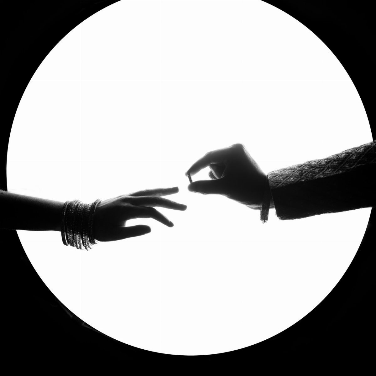 Silhouetted hands against a white circle with one person holding an engagement ring