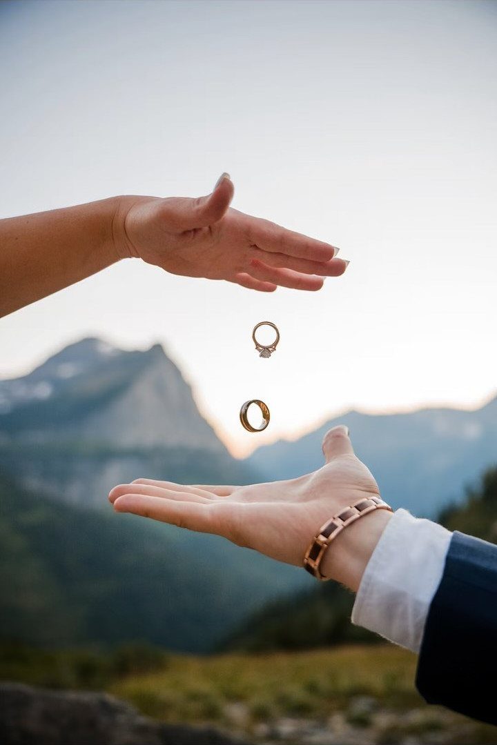 Two gold rings falling through the air between two open hands outdoors.