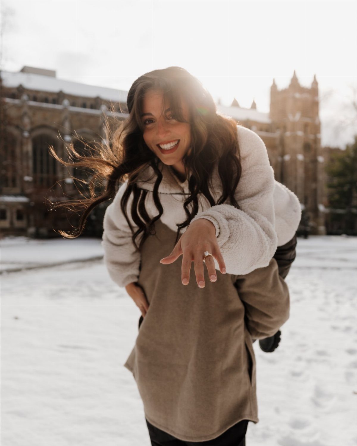 Smiling woman being carried on a man's back in snow showing engagement ring