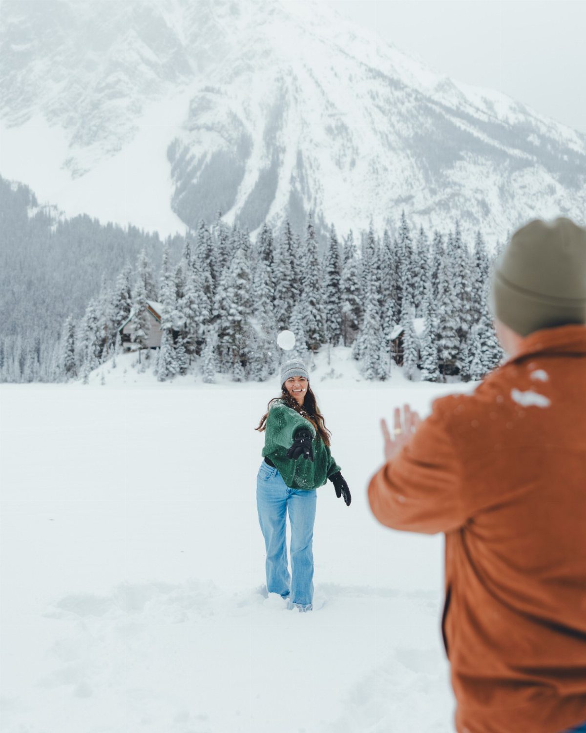 Couple playing in the snow with mountains and pine trees in the background