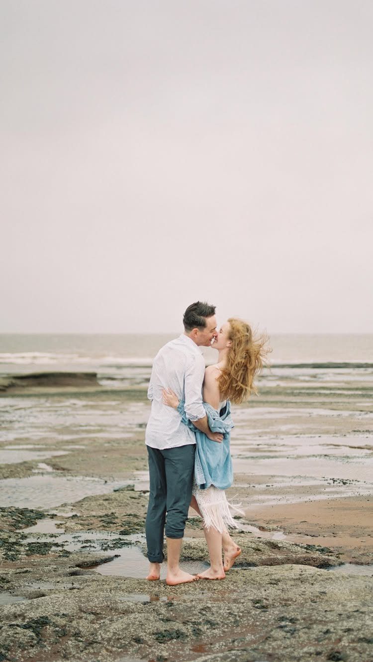 Couple kissing on a rocky beach with tide pools under an overcast sky