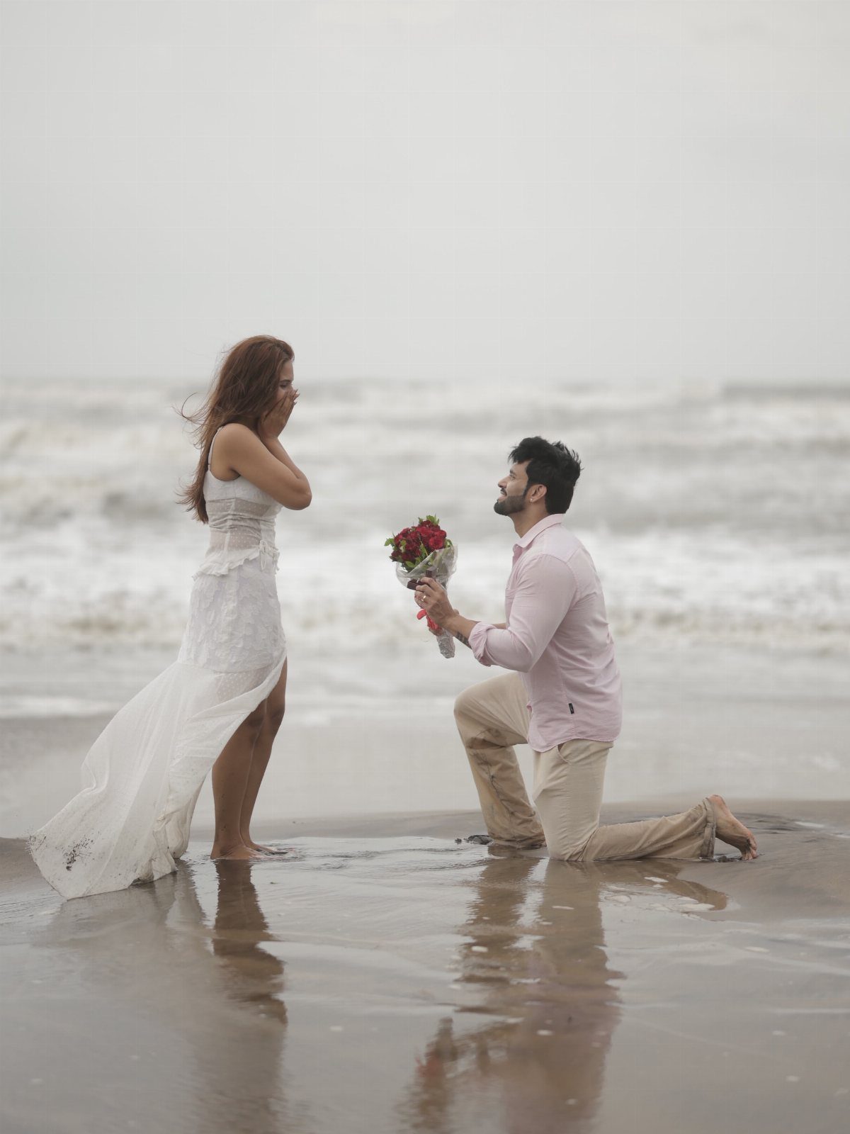 Man proposing to a woman on a beach with reflections on wet sand