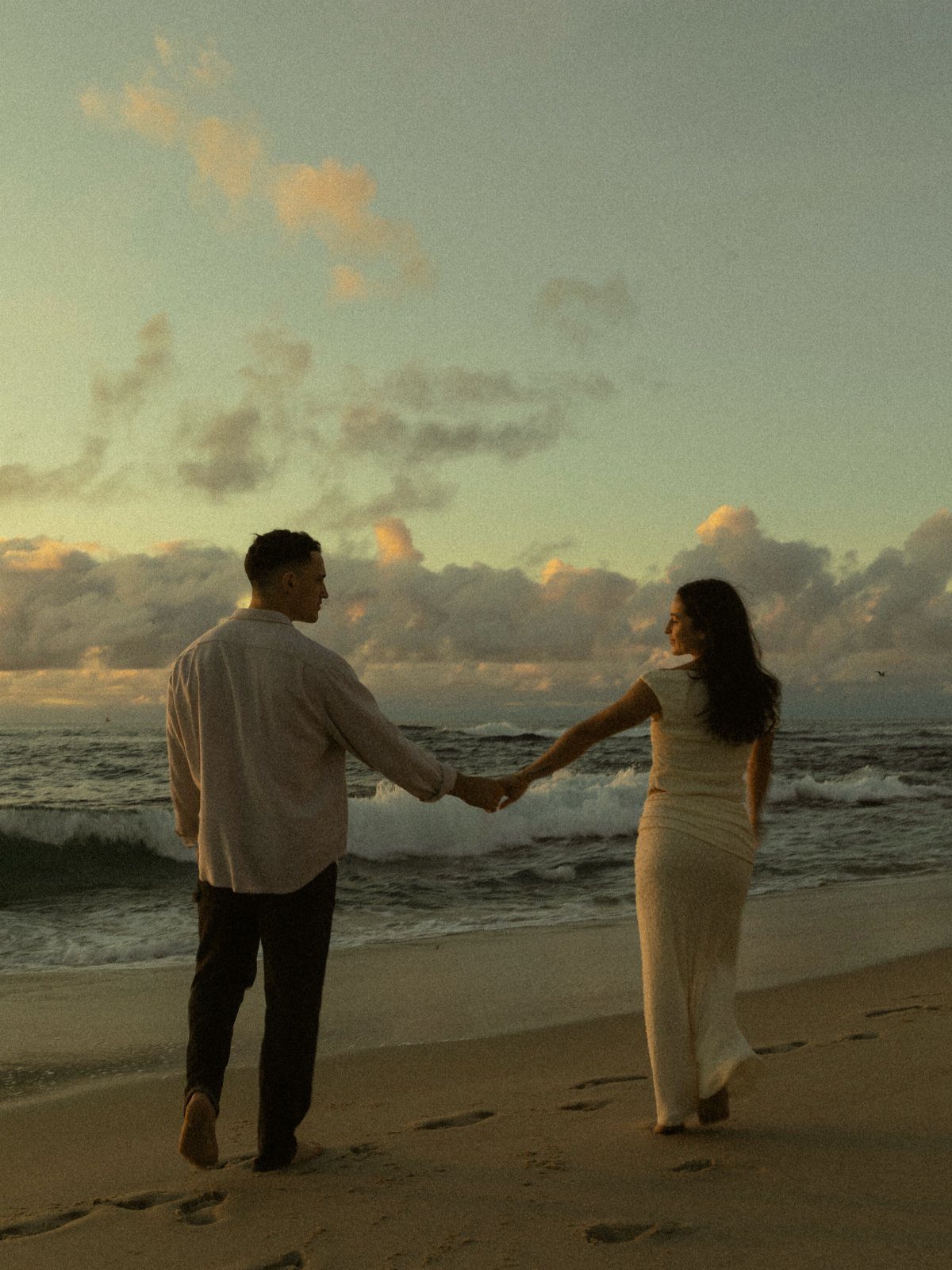 Couple holding hands while walking along the waterline on a sandy beach at sunset