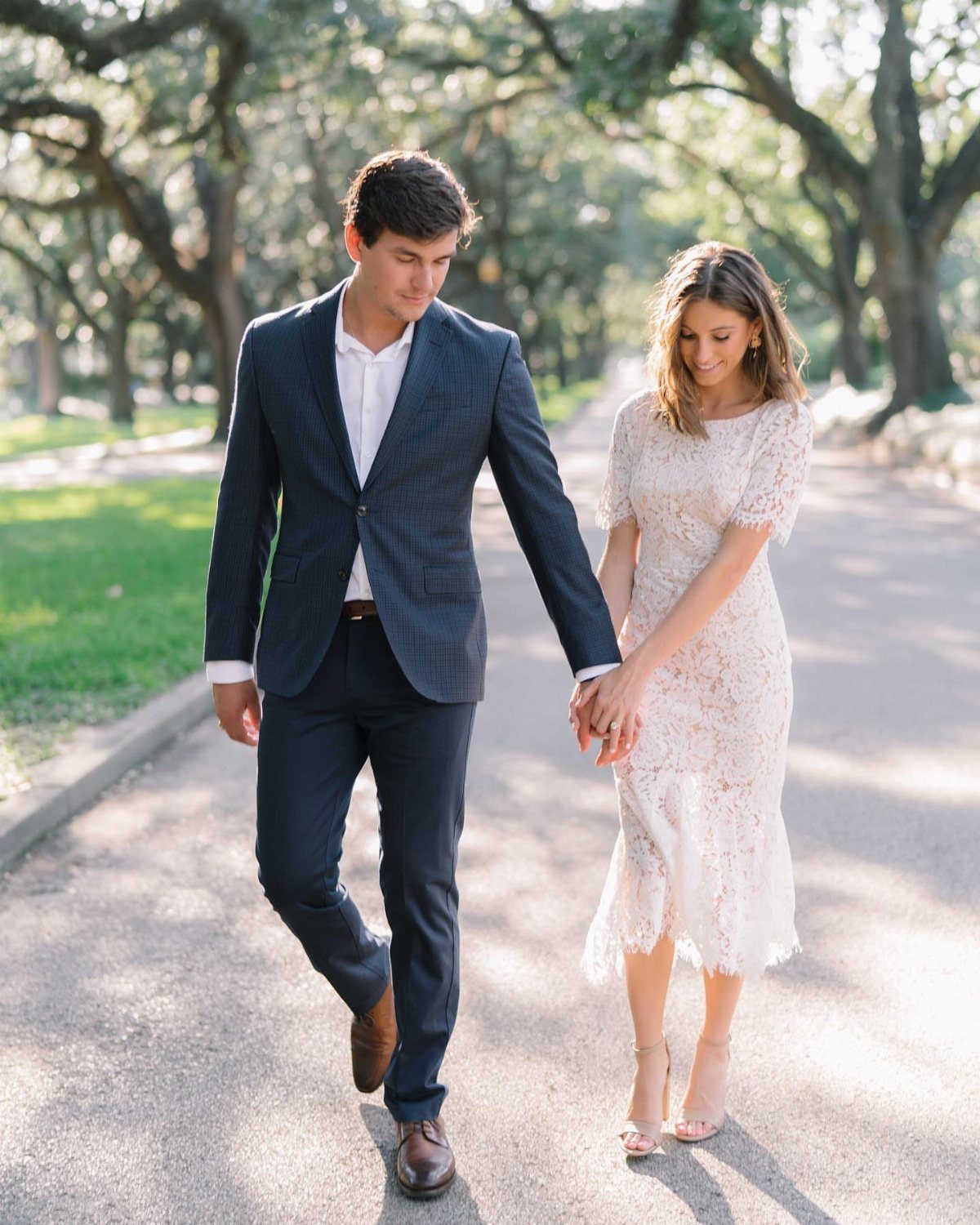 Couple holding hands walking in a park, woman wearing a white lace midi dress