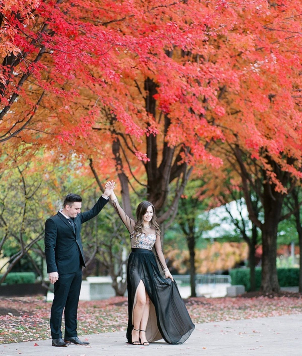 Couple posing under red autumn leaves, woman wearing a long black dress.