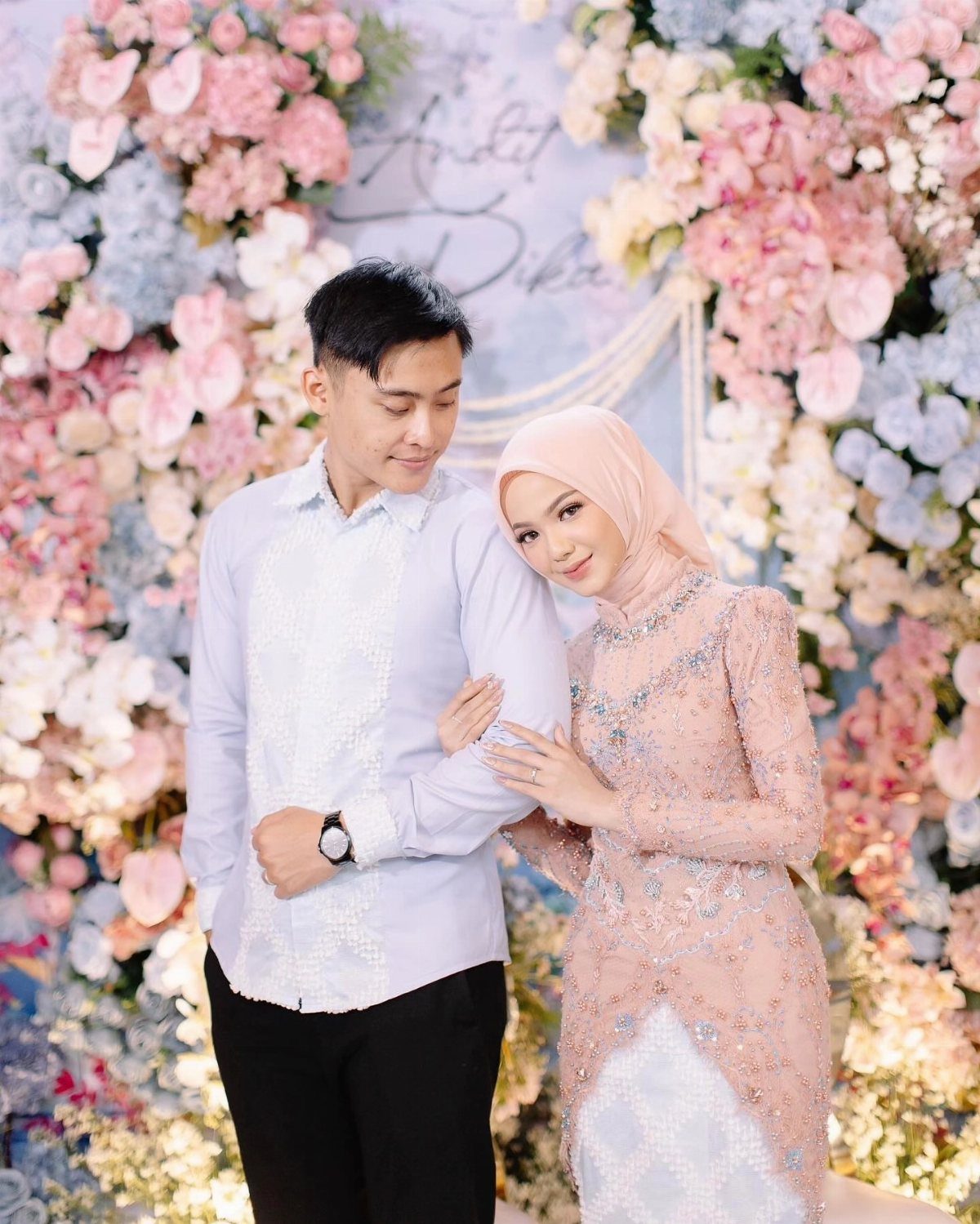 Couple in light blue and blush pink outfits posing before a floral wall.