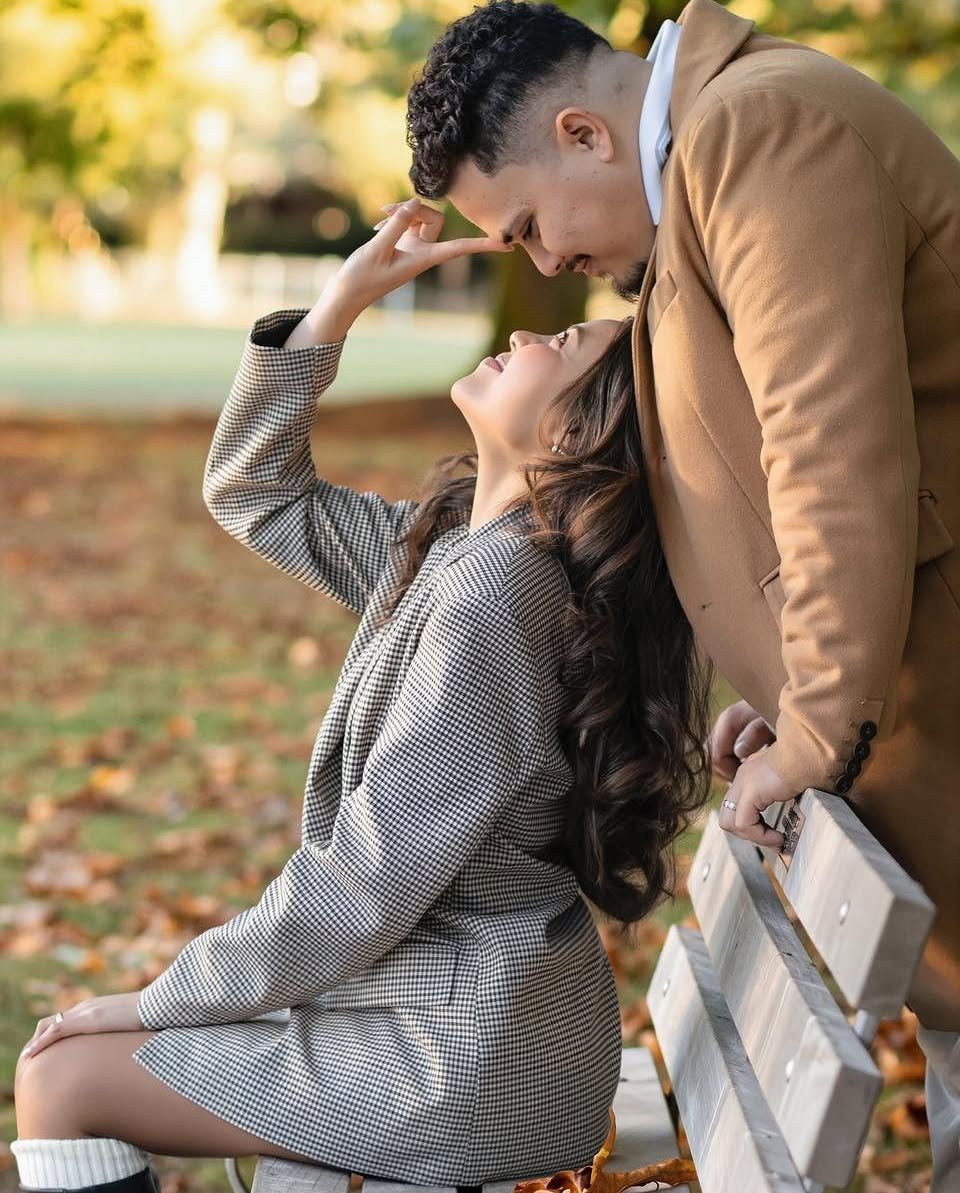 Couple in autumn attire posing together outdoors with fallen orange leaves around them.