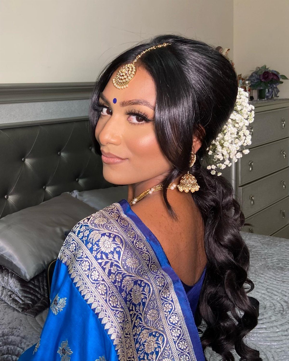 Woman with professional makeup and styled hair wearing a blue gold sari