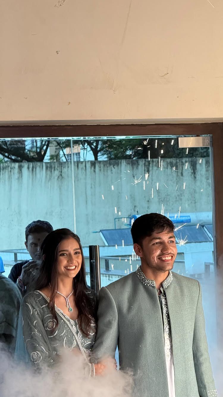 Smiling couple in coordinated light sage green traditional Indian formal attire posing together.