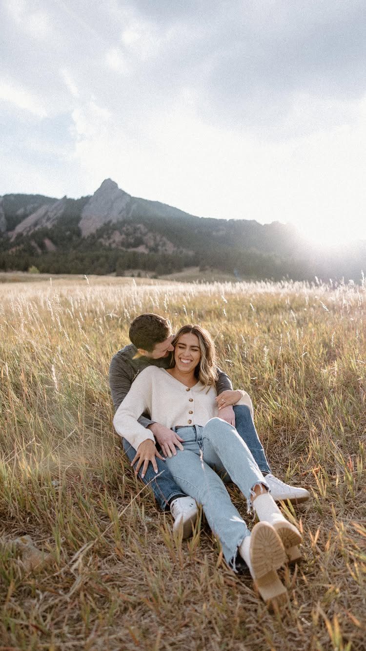 Couple sitting in a golden field wearing casual sweaters and blue jeans.