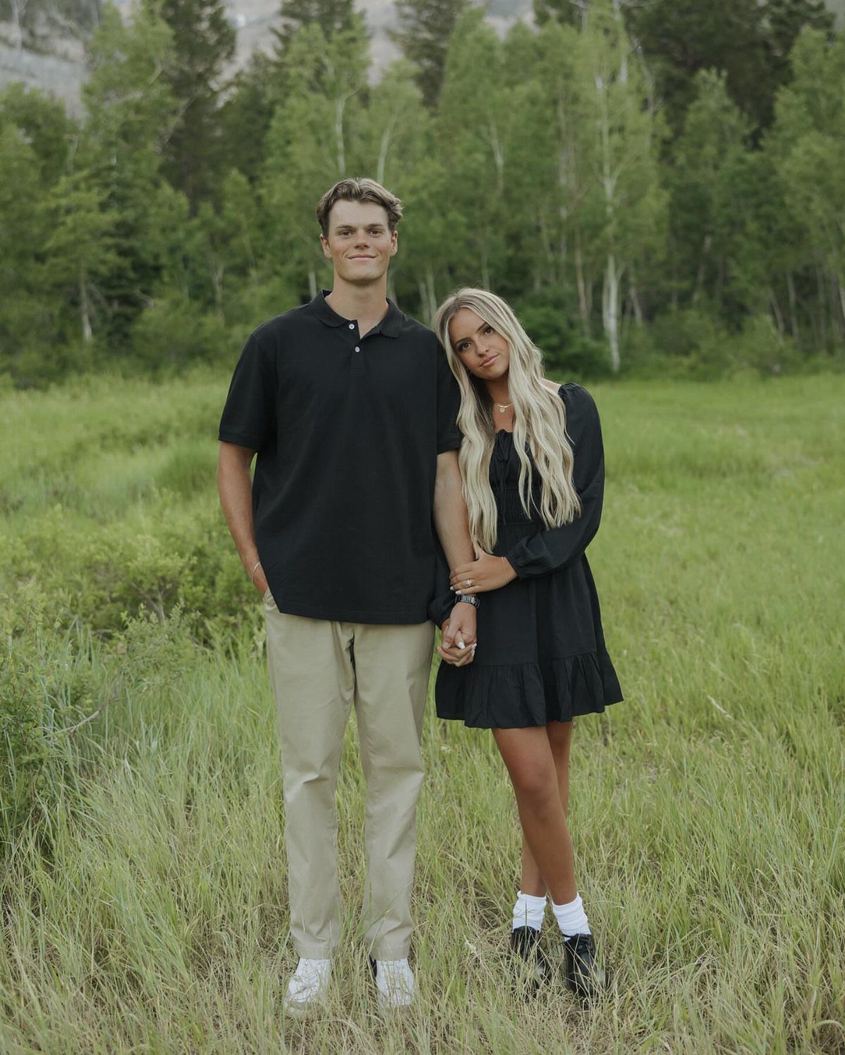 Young couple holding hands in a field wearing coordinated black and khaki outfits.