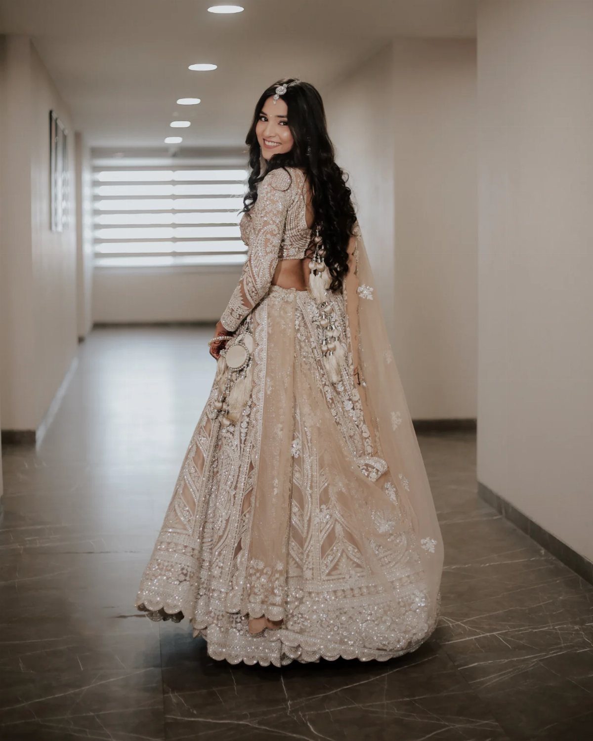 Woman in an ornate cream lehenga posing in a white modern hallway