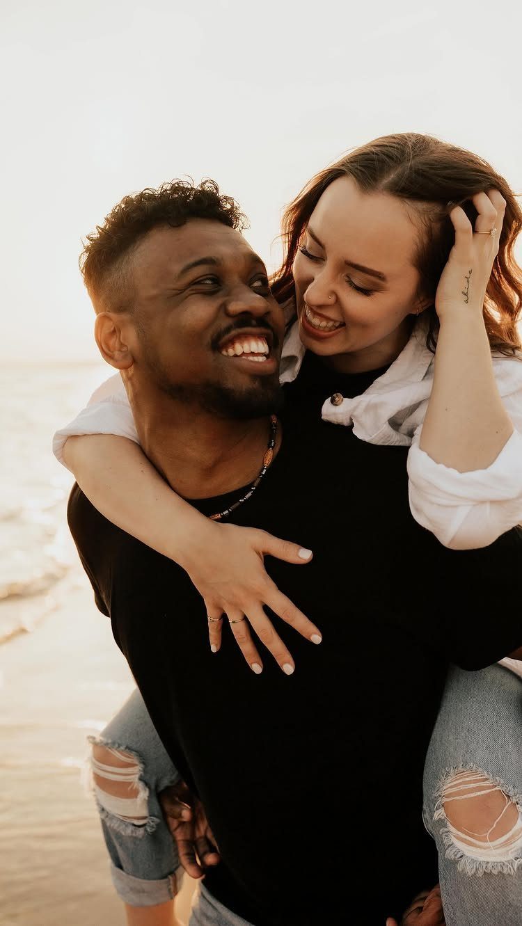 Smiling couple on a beach with the man giving the woman a piggyback ride.