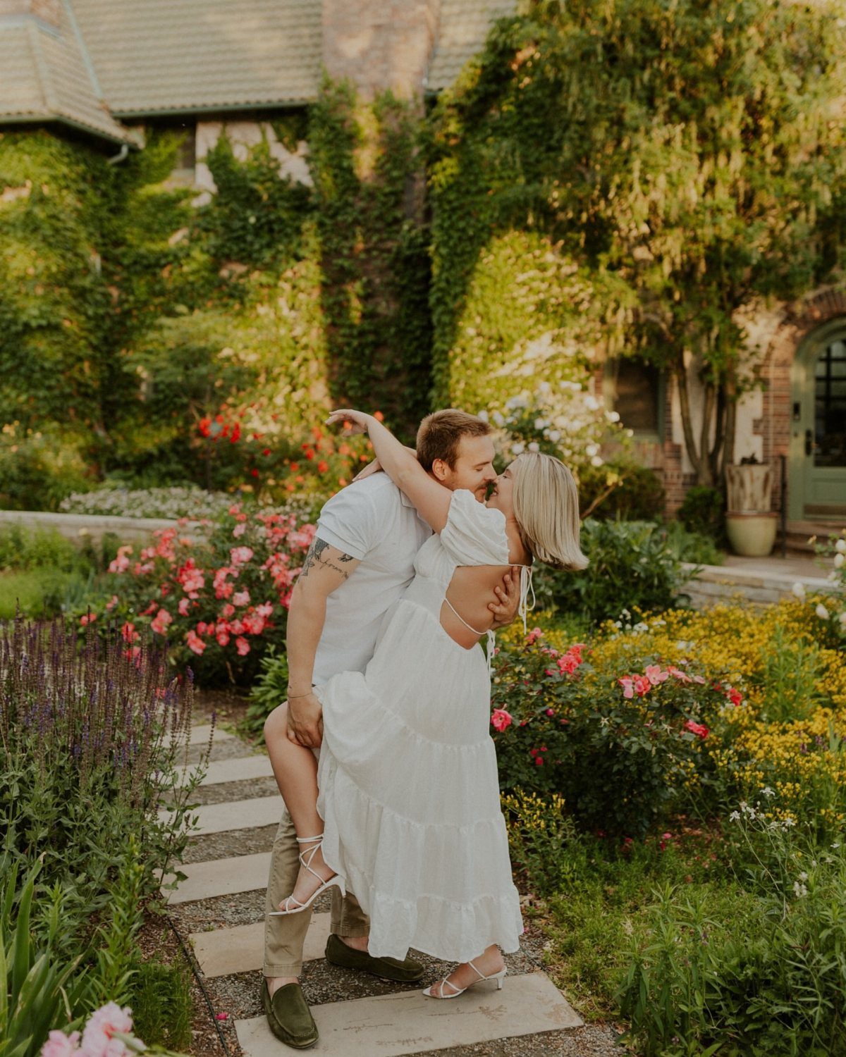 Couple kissing in a vibrant botanical garden with colorful flowers and stone path.
