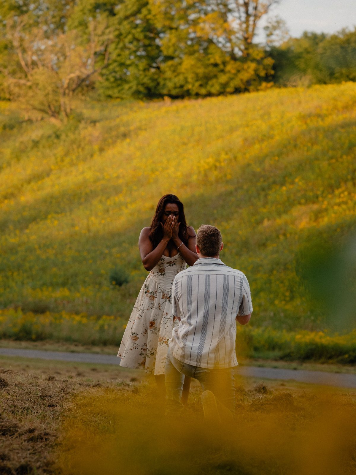 Man proposing to a woman in a field of yellow wildflowers during golden hour.
