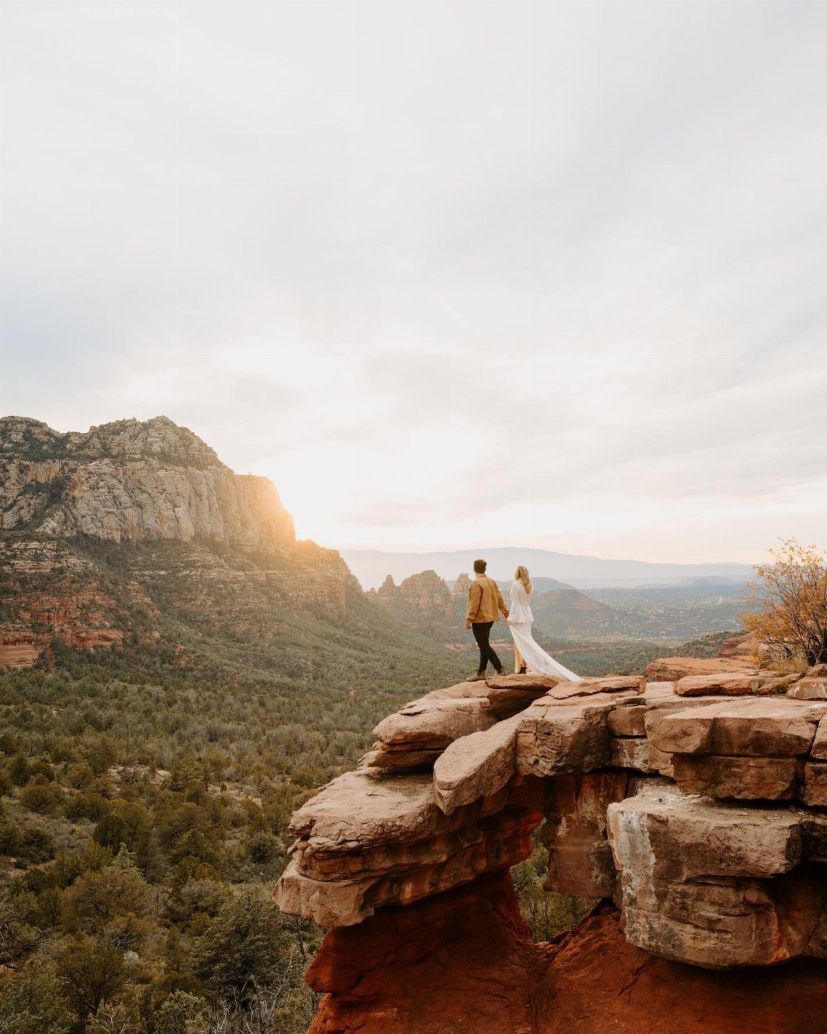Couple standing on a red rock cliff overlooking a scenic mountain valley landscape