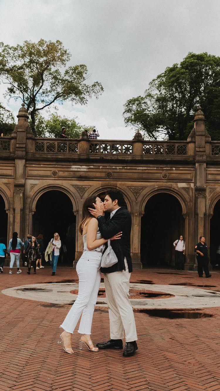 Couple kissing in front of a stone arched terrace in a public park.