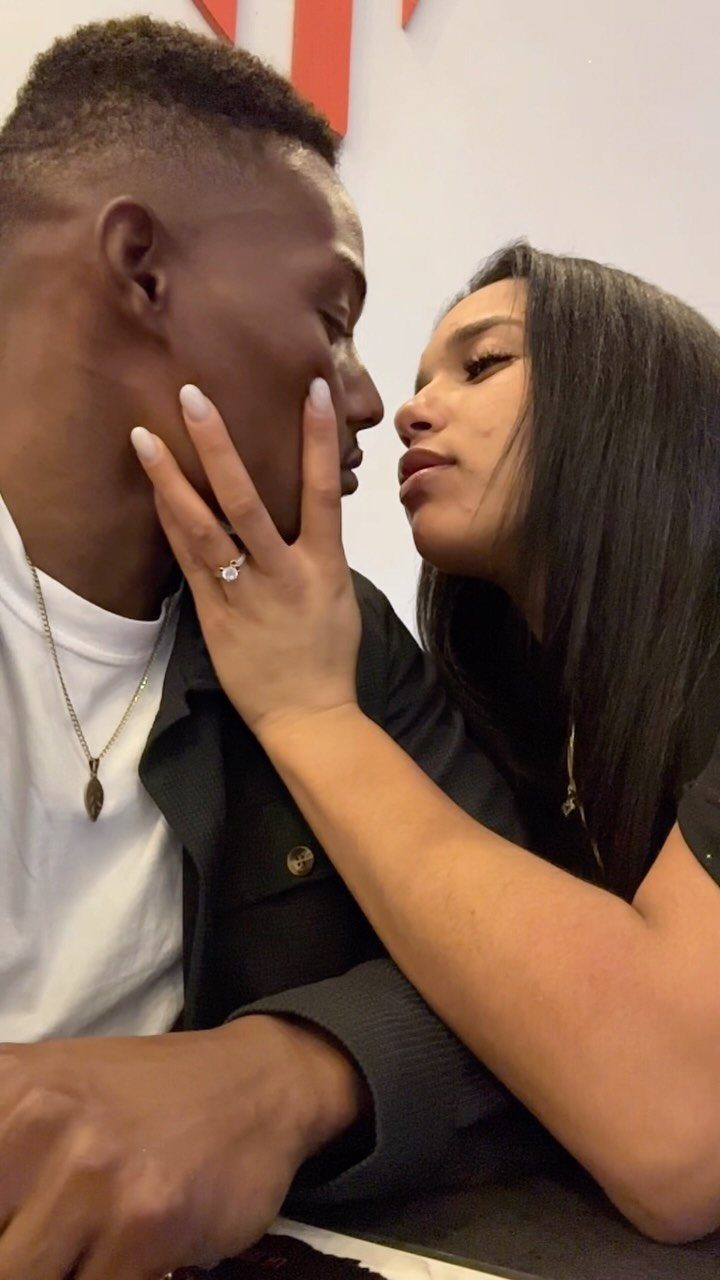 Couple facing each other closely for an almost kiss, showing an engagement ring.