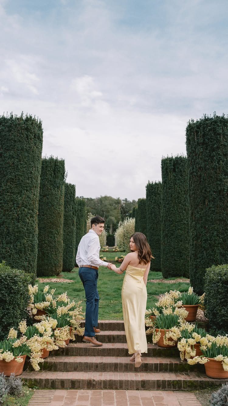 Couple holding hands while walking up stone steps in a formal manicured garden.