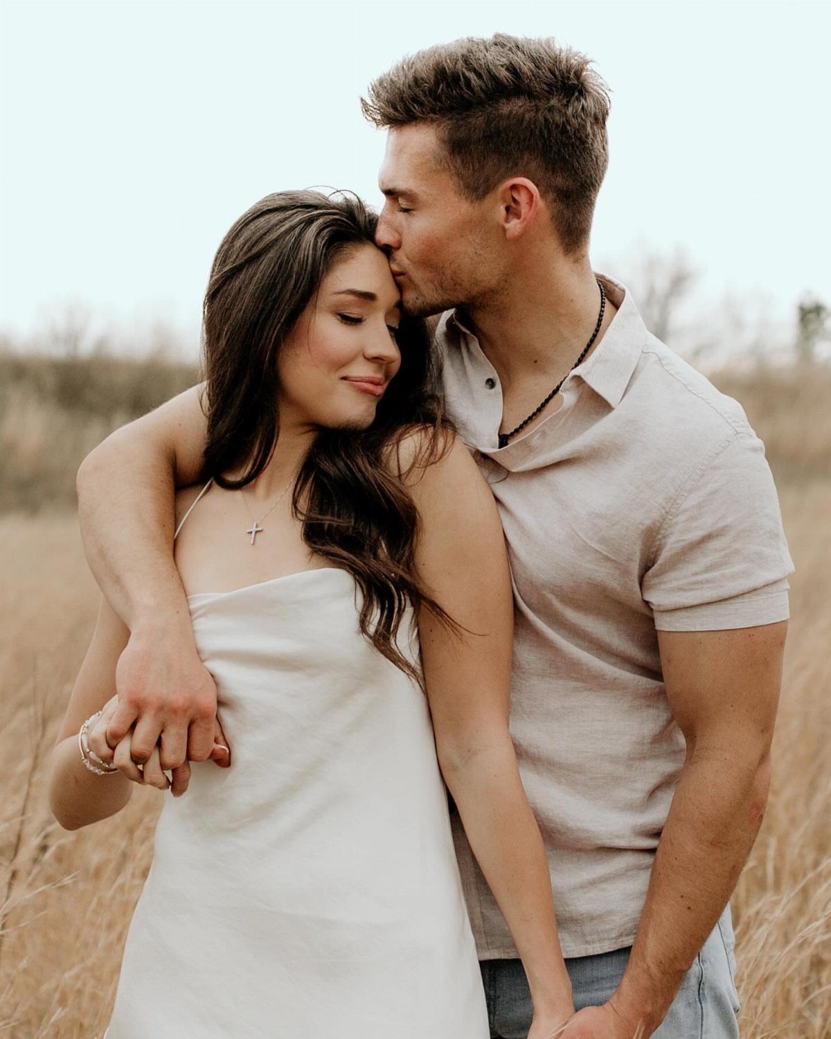 Man kissing woman's temple while embracing in a golden grassy field