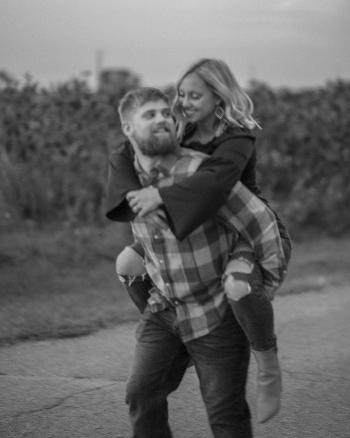 Man giving a woman a piggyback ride while both smile in a field.
