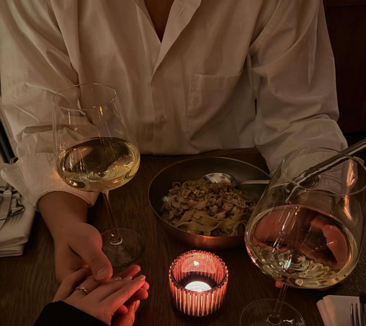 Couple holding hands at a dinner table with white wine and pasta.