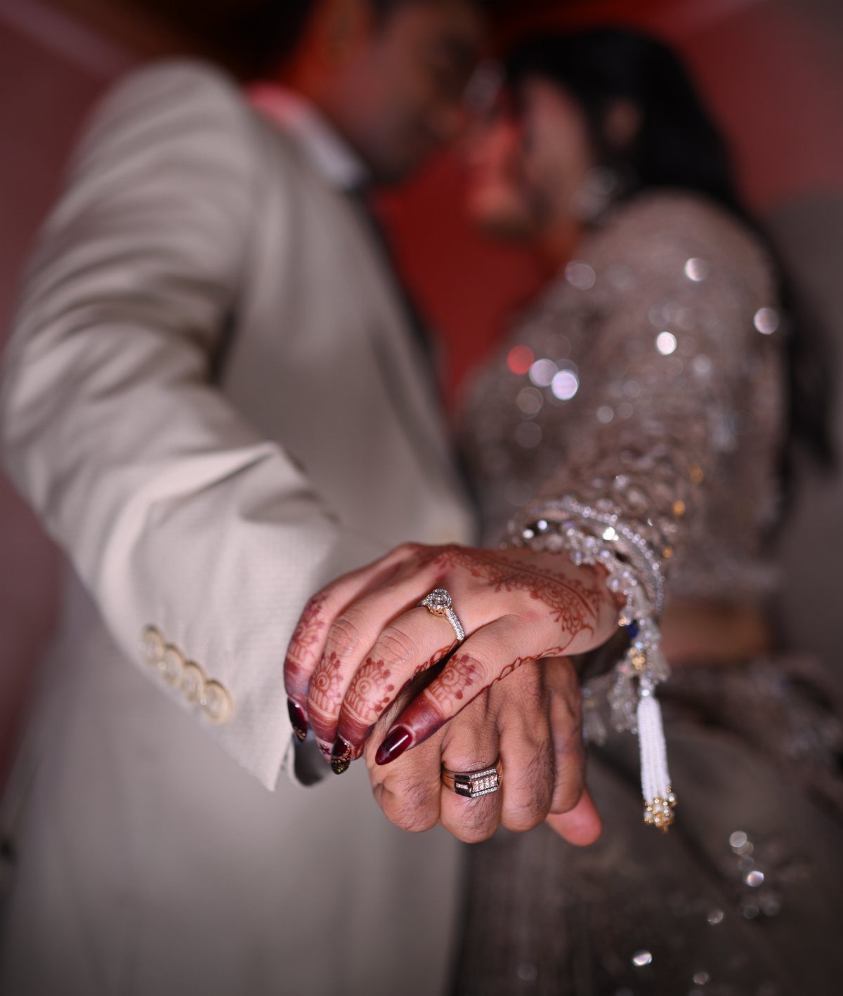 Couple holding hands showing engagement rings with henna and sparkling silver attire