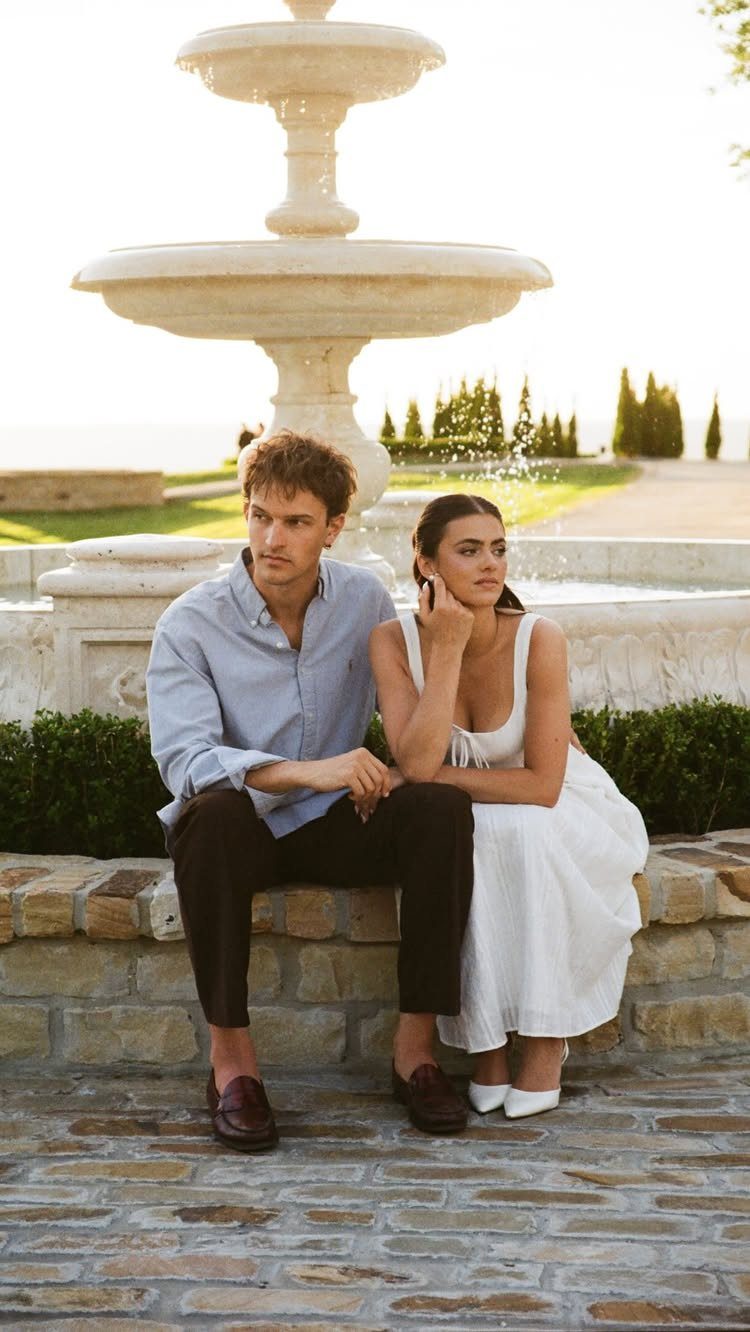 Man and woman sitting on a stone ledge in front of a white fountain.