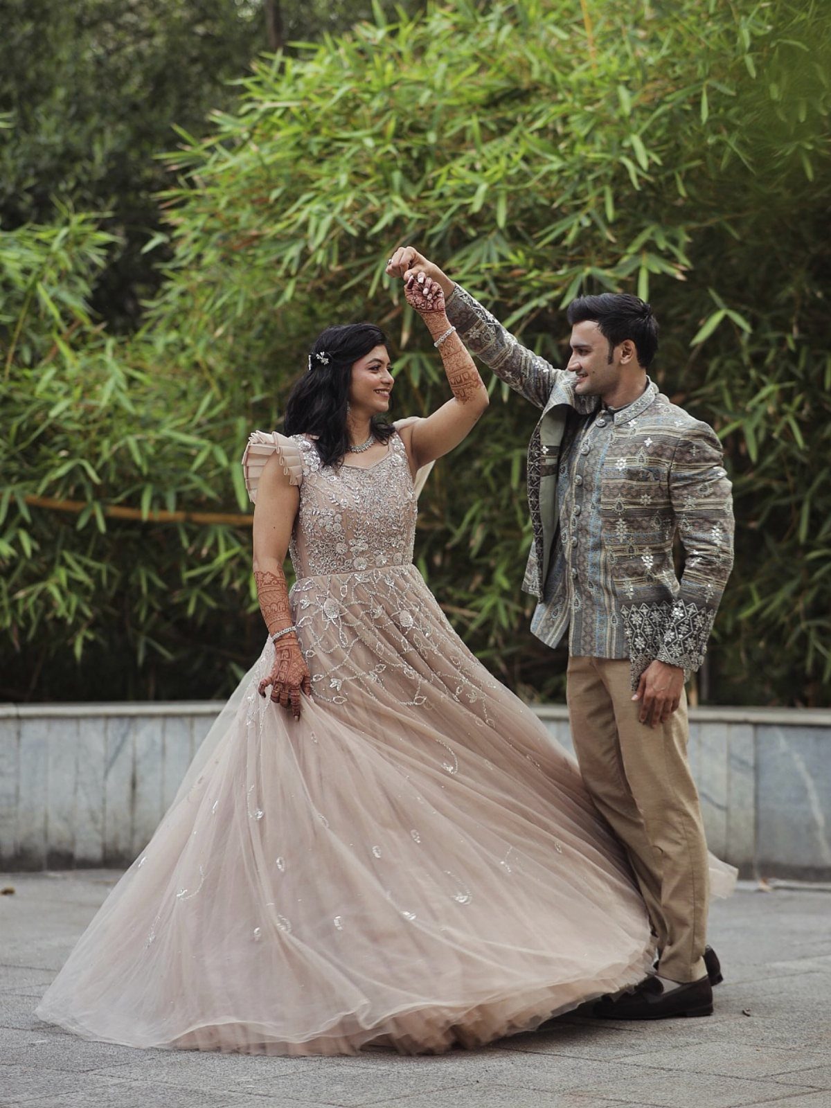 Couple in formal wear twirling together outdoors with green bamboo in the background