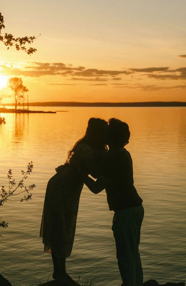 Couple kissing in silhouette against a golden sunset over a calm lake.