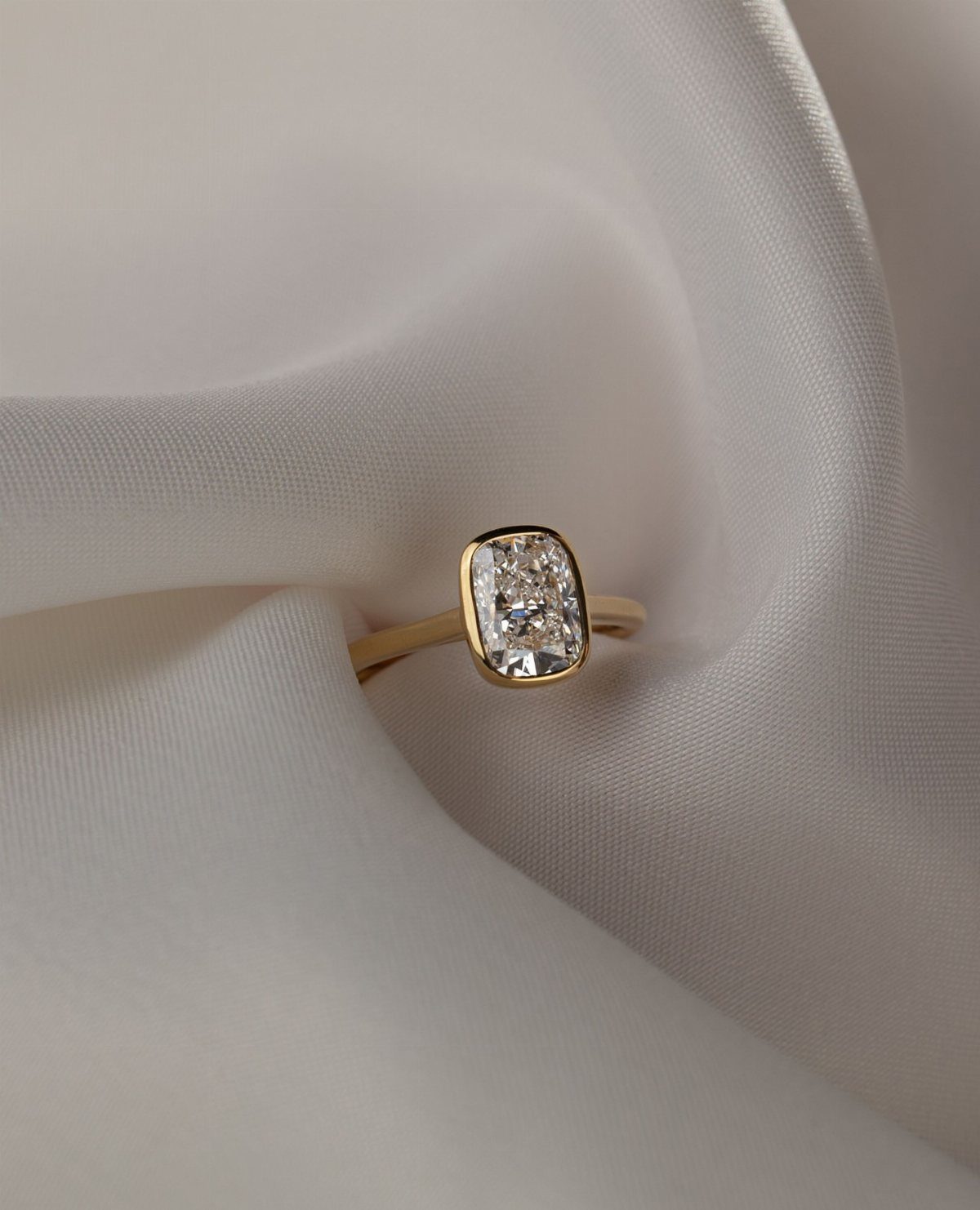 Gold bezel set ring with a rectangular diamond on white satin fabric
