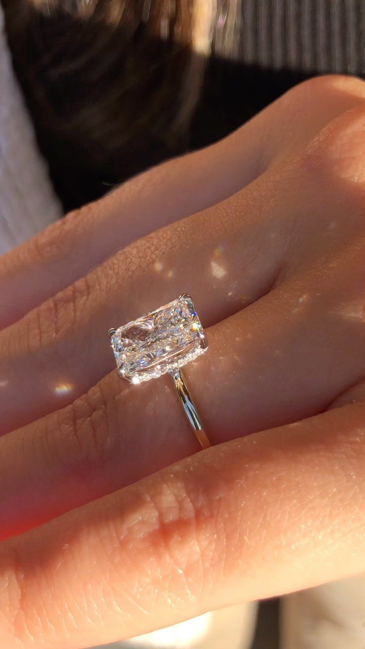 Gold engagement ring with a large emerald-cut diamond on a person's finger