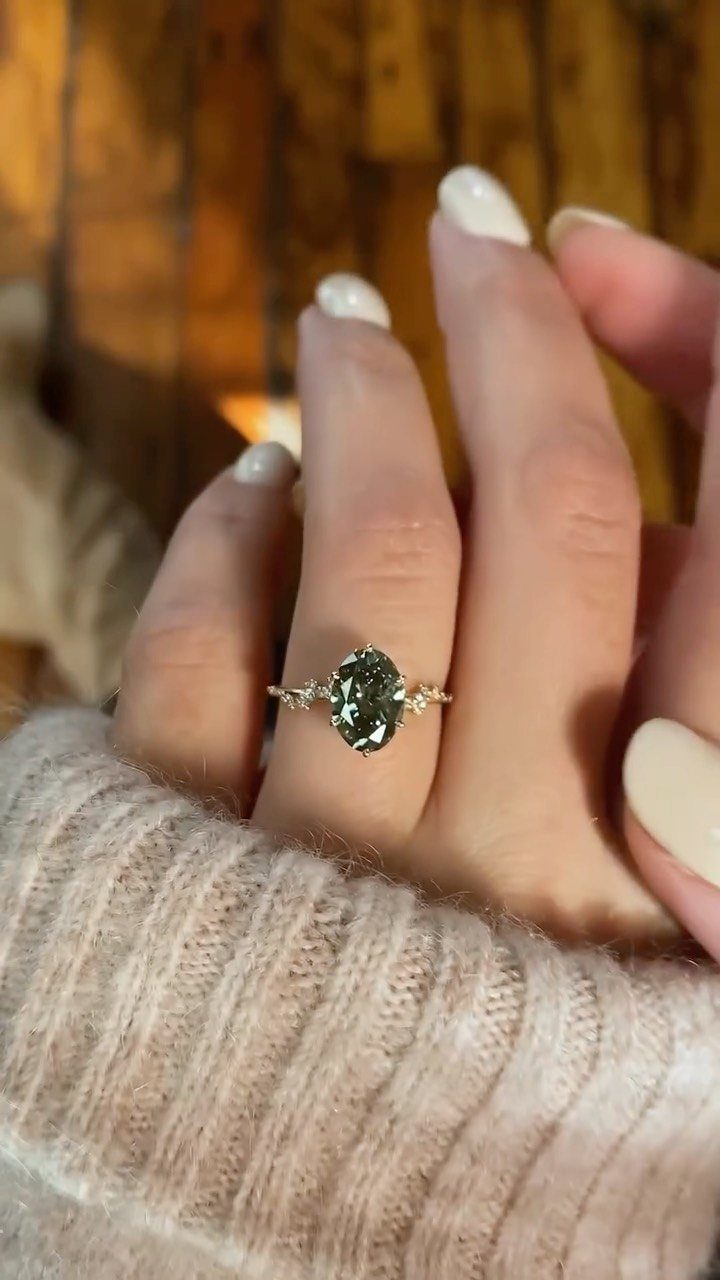 Gold ring with an oval green gemstone on a finger with white nails