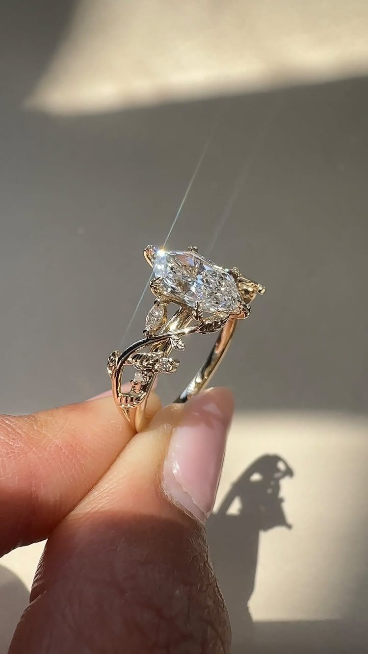 Gold engagement ring with pear-shaped diamond and leaf-inspired vine band held by fingers