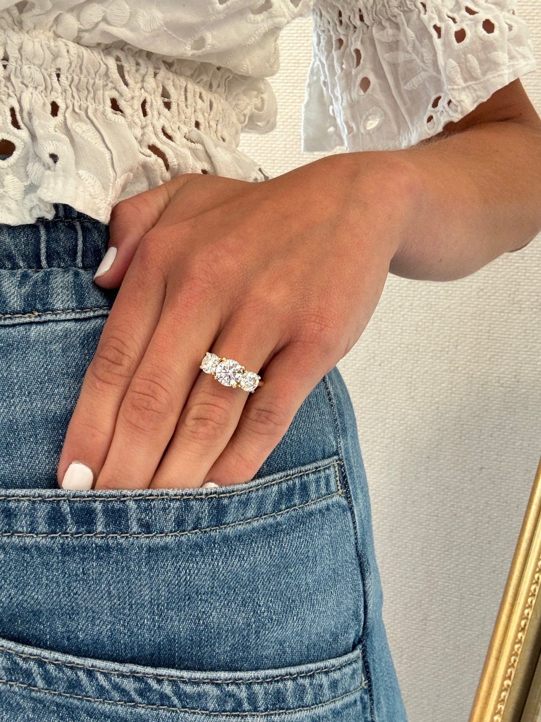 Three-stone gold engagement ring on a hand resting on blue denim jeans