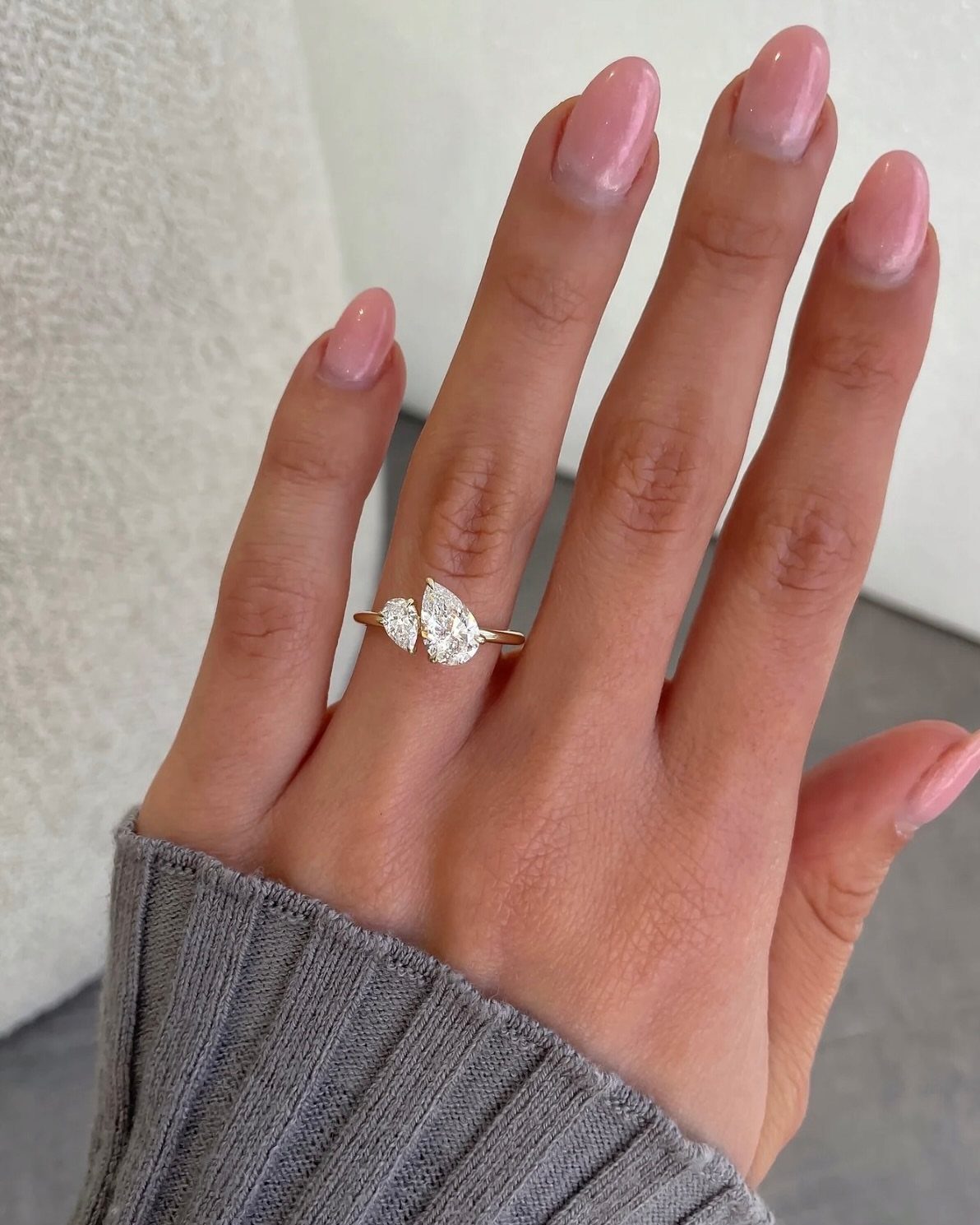 Gold ring with two pear-shaped diamonds on a hand with pink nails