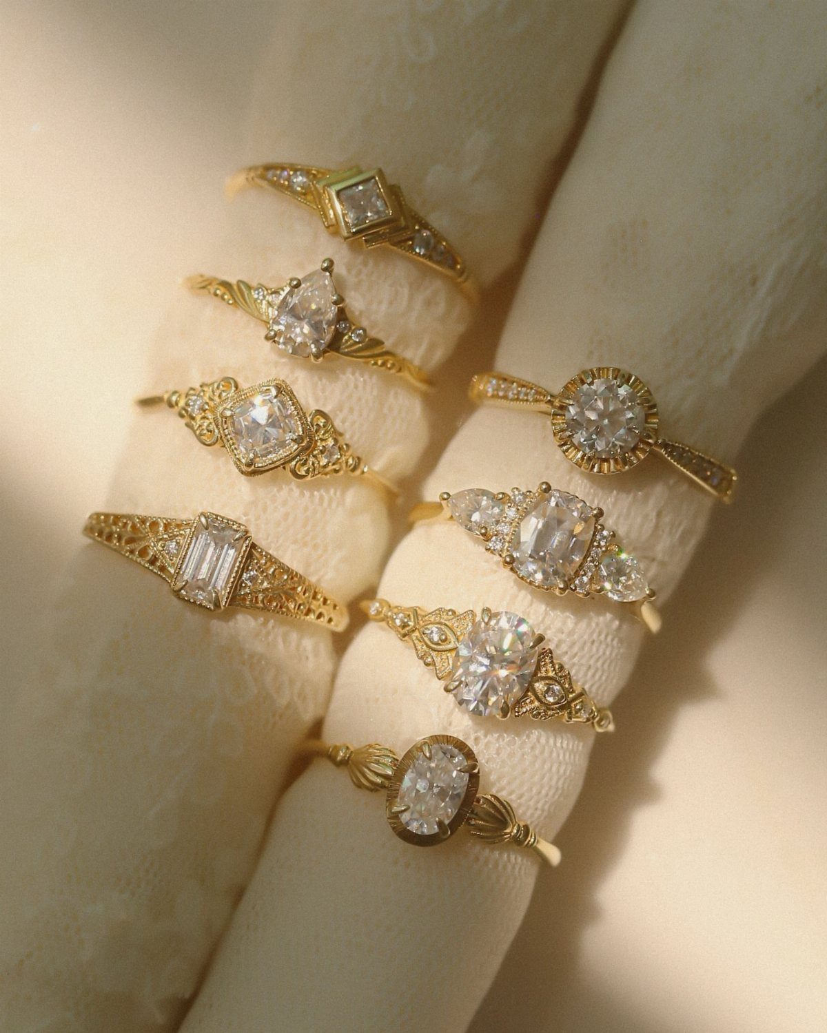 Gold engagement rings with vintage filigree details displayed on white velvet holders.