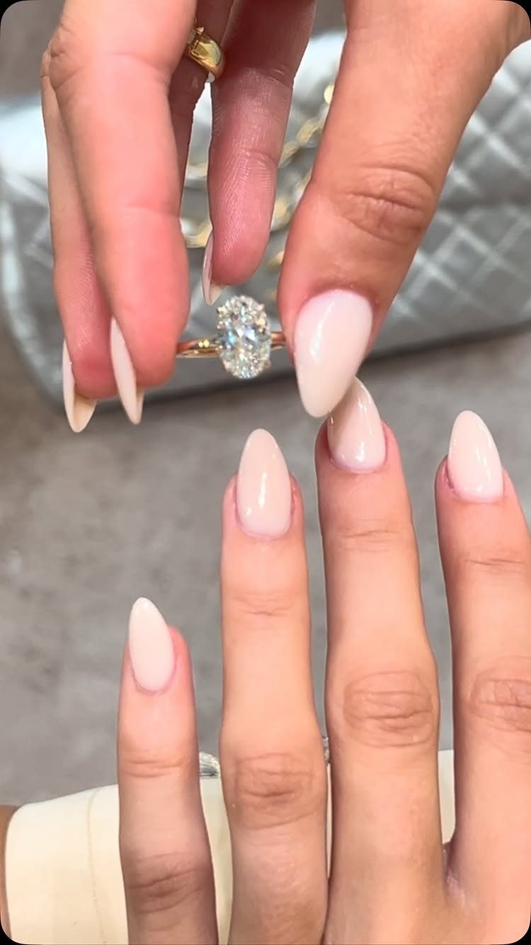 Gold engagement ring with a large oval diamond held by manicured fingers