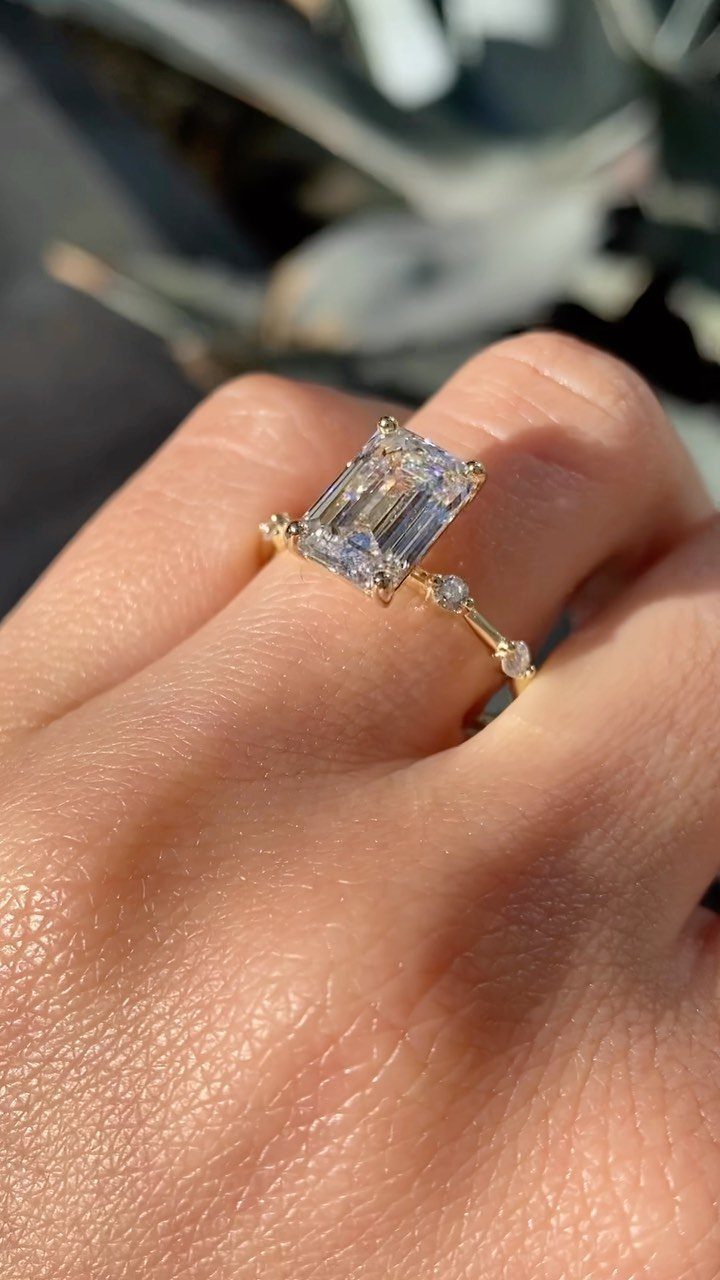Gold engagement ring with a large emerald-cut diamond on a person's finger.