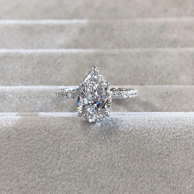 Pear-shaped diamond engagement ring with a pavé band on grey velvet fabric