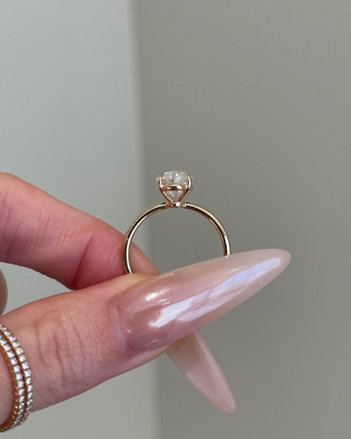 Gold engagement ring with a large round diamond held by manicured fingers.