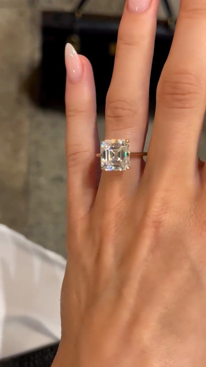 Gold engagement ring with a square Asscher cut diamond on a finger