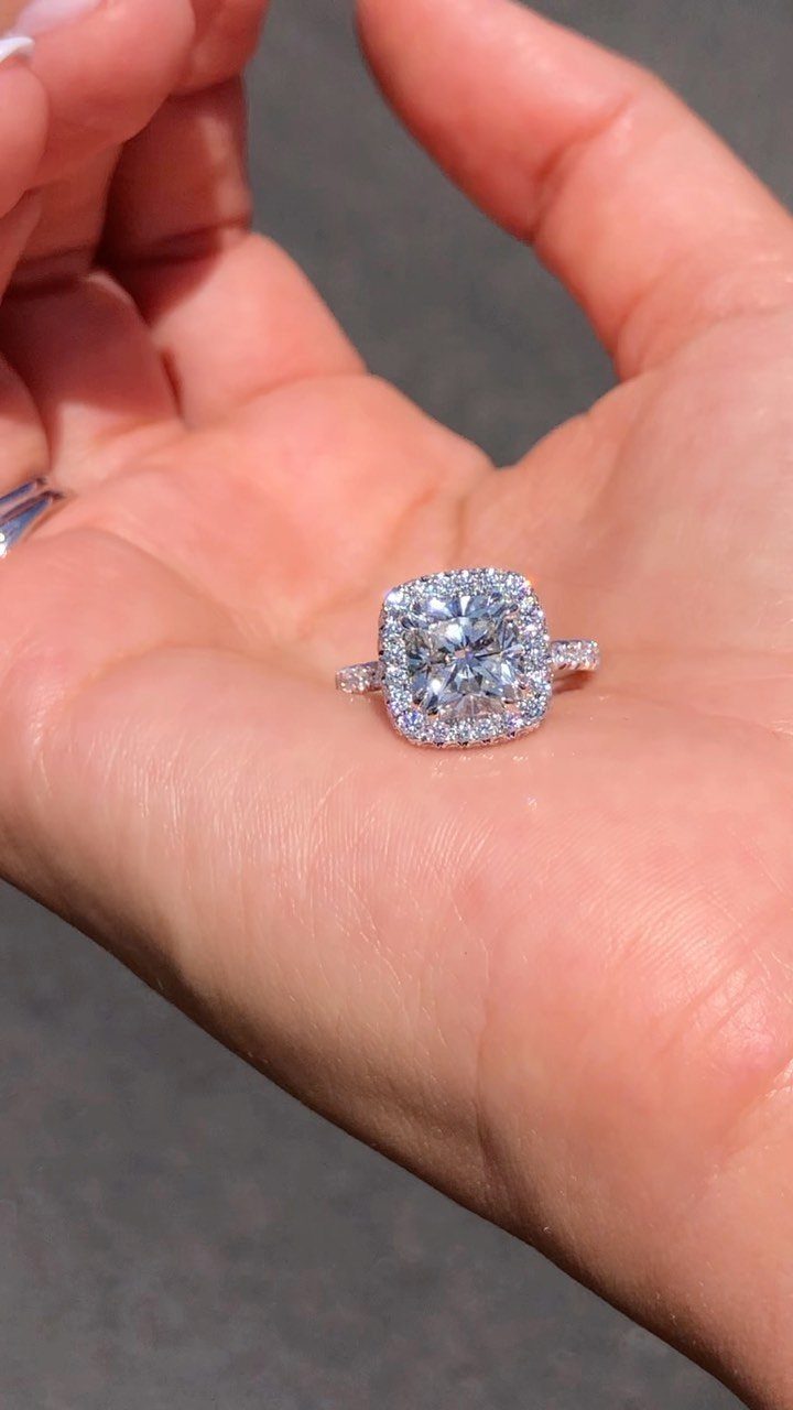 Cushion cut diamond engagement ring with a halo resting on a palm.