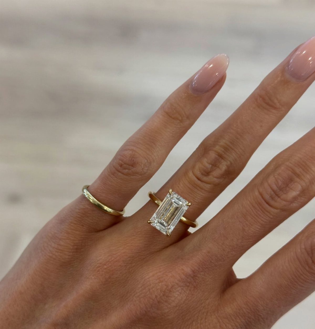 Emerald-cut diamond engagement ring and gold band on a woman's finger