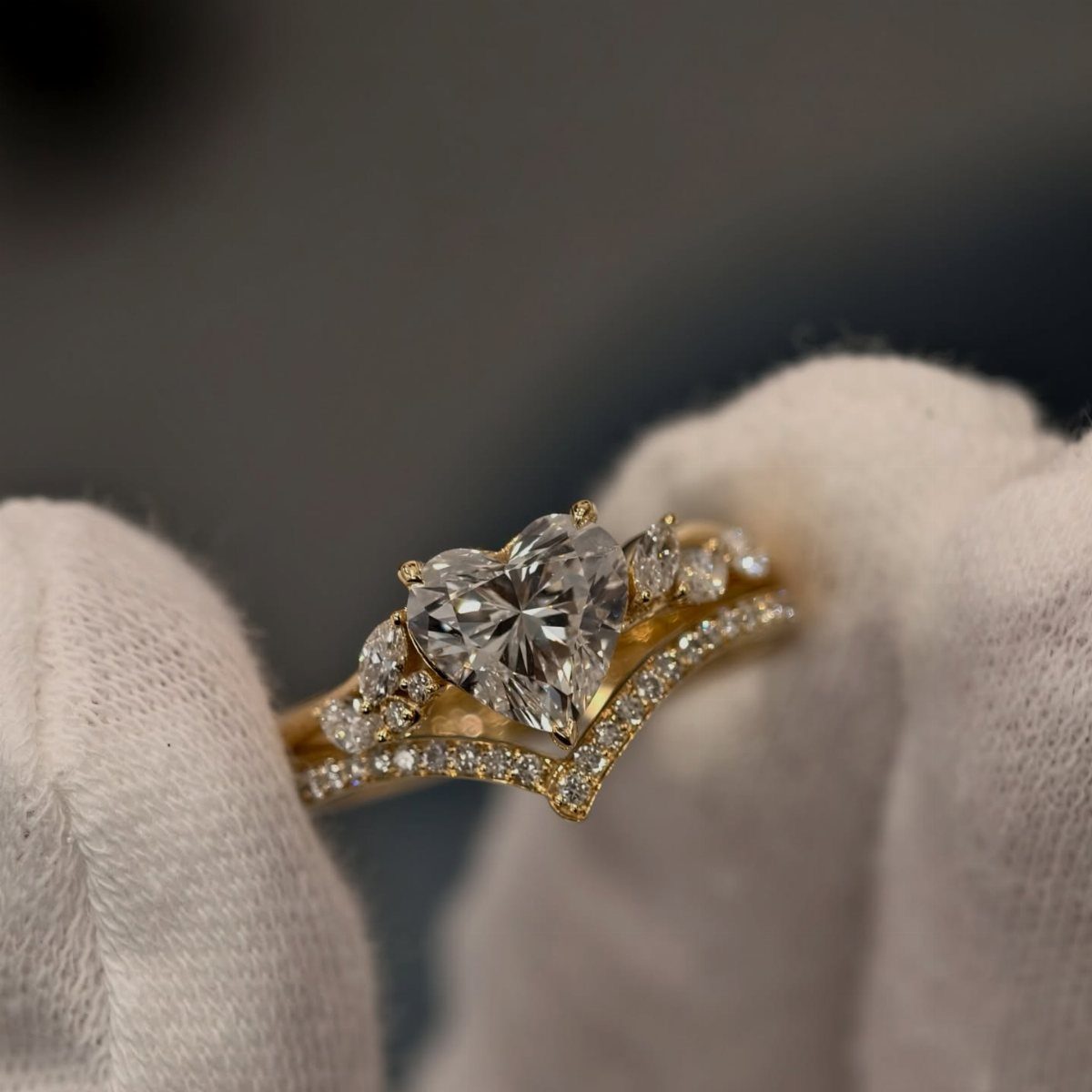 Heart-cut diamond engagement ring with gold band held by gloved fingers.