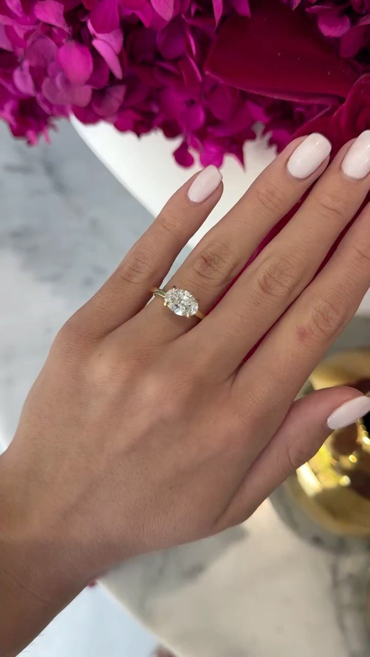 Gold engagement ring with an oval cut diamond on a manicured finger