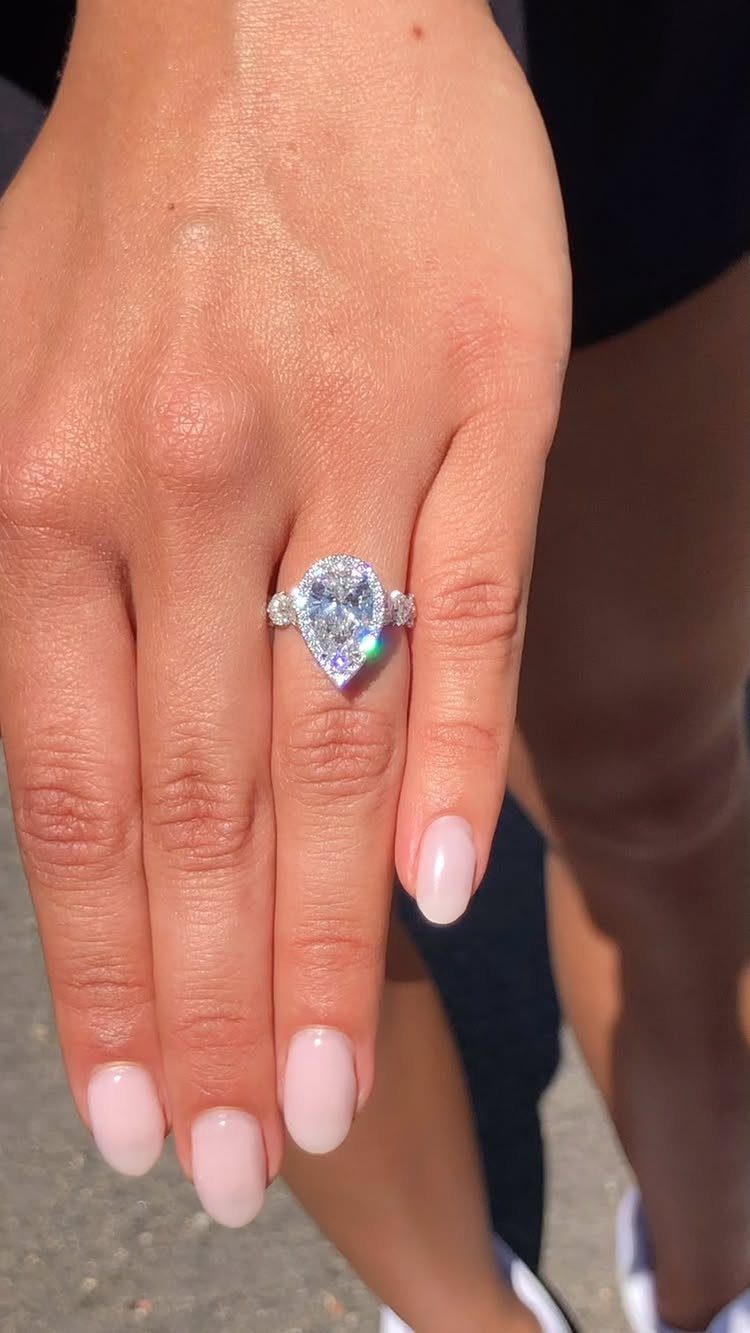 Pear-shaped diamond engagement ring on a hand with light pink manicured nails.